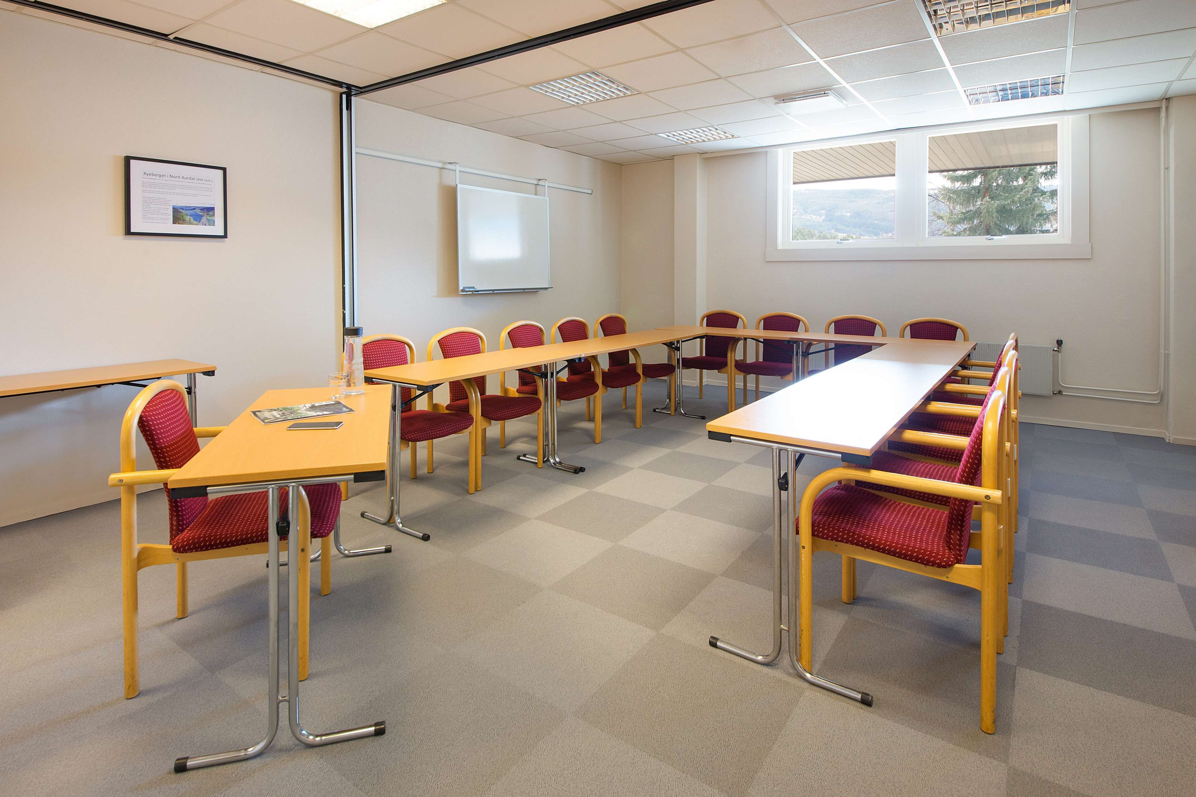 A conference room with a long table, red and yellow chairs, a projector screen, and a window with a view.