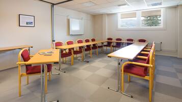 A conference room with a long table, red and yellow chairs, a projector screen, and a window with a view.