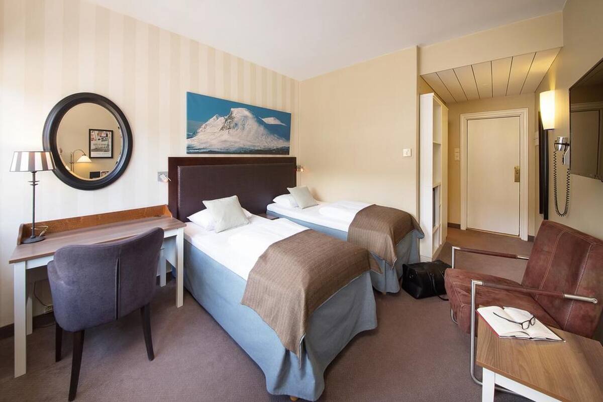 A hotel room with two beds, a desk, a chair, a mirror, and a painting on the wall.