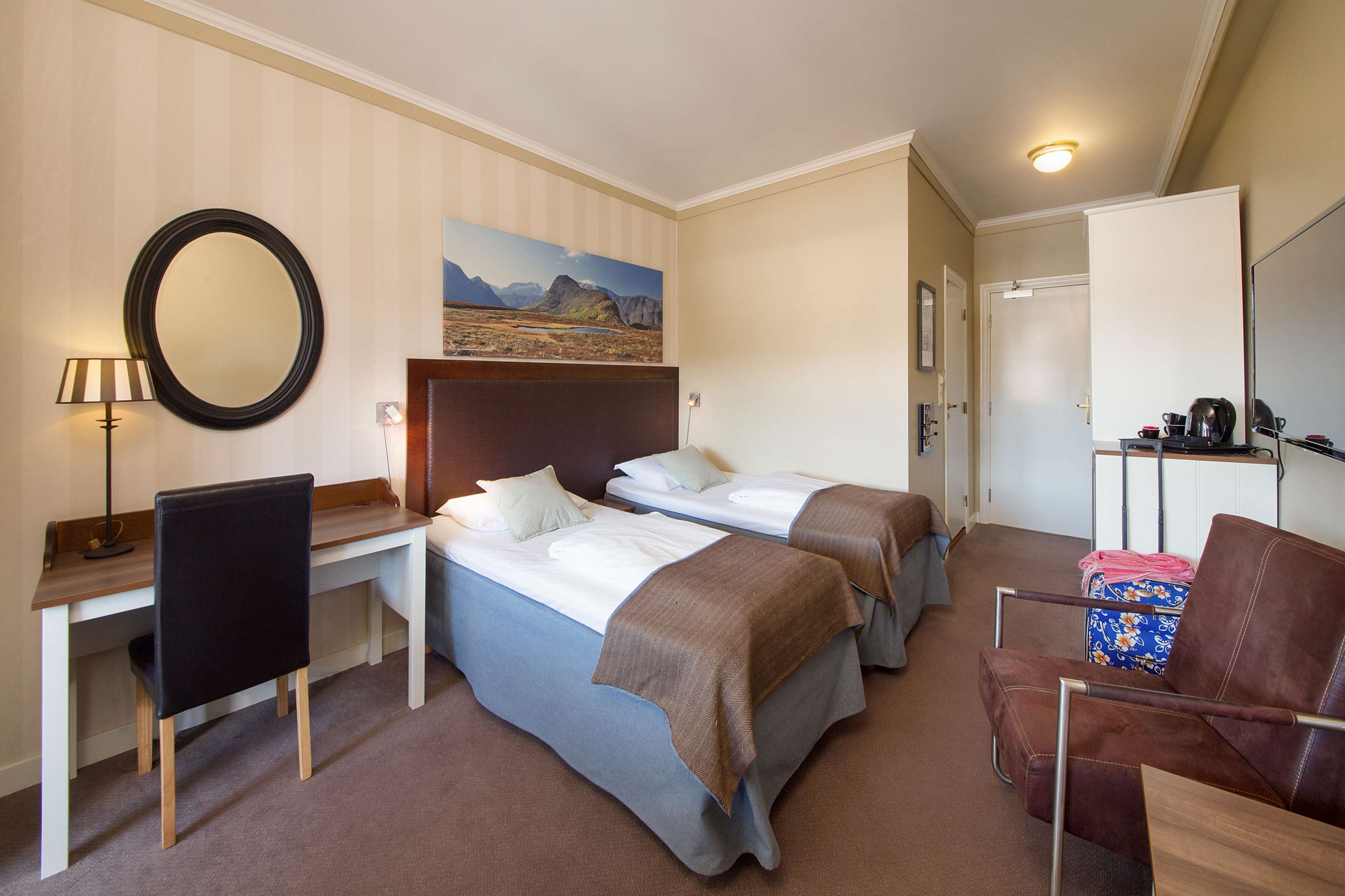 Ein Hotelzimmer mit zwei Betten, einem Schreibtisch, einem Stuhl, einem Spiegel und einem Bild an der Wand.