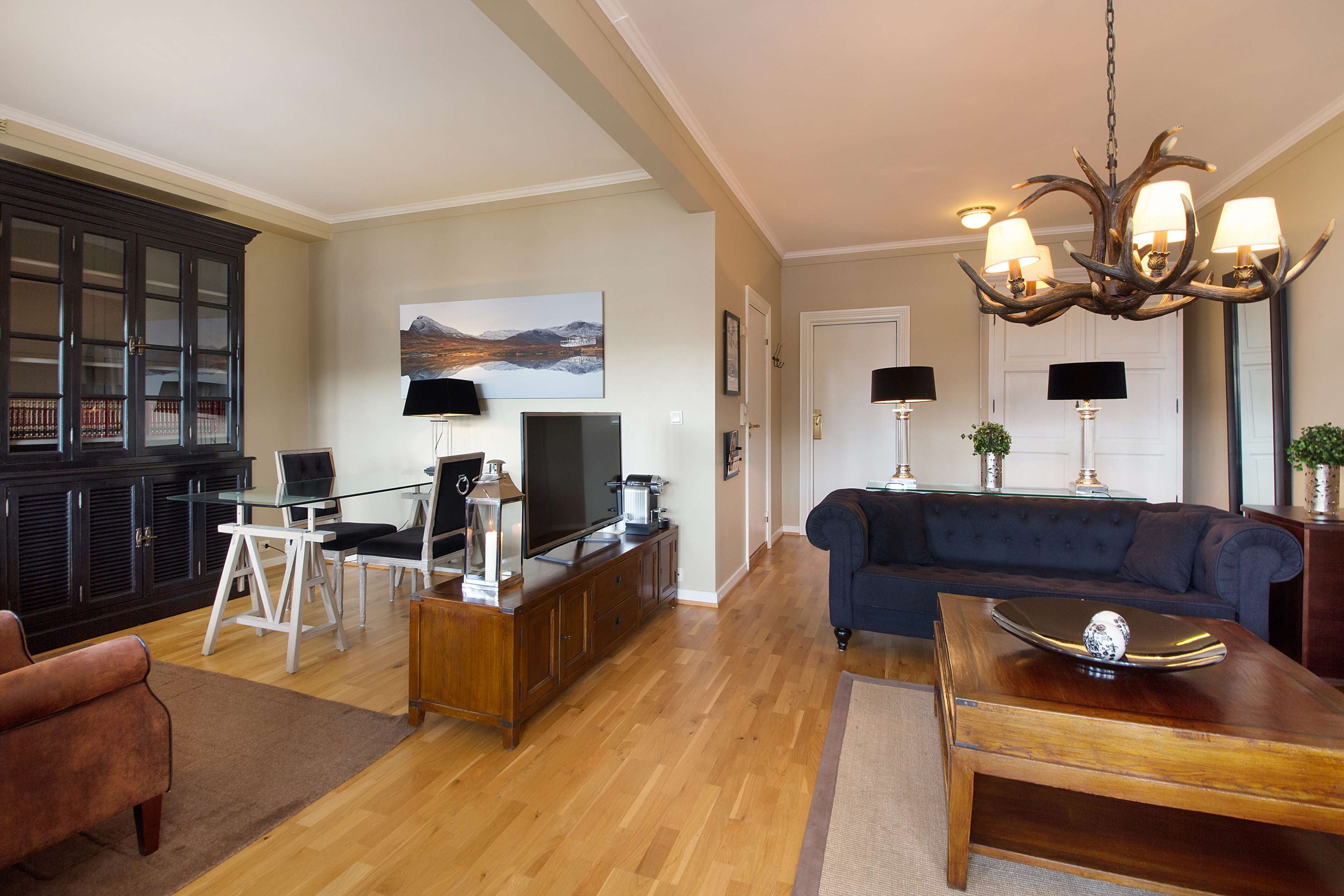 A living room with a dark blue sofa, a wooden coffee table, a television on a wooden stand, a chandelier, and a large cabinet.