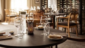A restaurant setting with round tables, wine glasses, and a wine rack in the background. - Scandic Valdres (Nord-Aurdal)