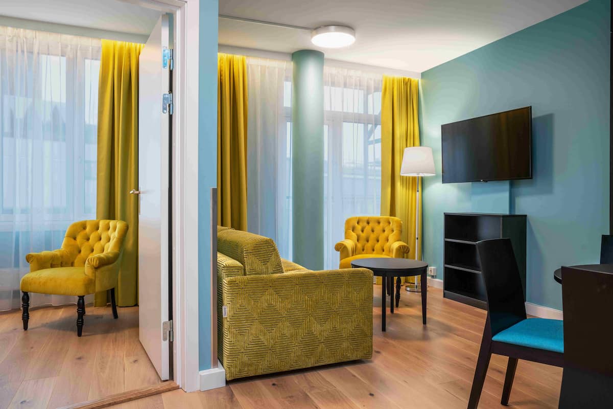 Una habitación de hotel con sofá, sillones, televisor y lámpara.