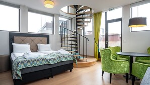 A modern hotel room with a spiral staircase, a bed with a patterned blanket, green upholstered chairs, and a small table. - Thon Hotel Slottsparken (Oslo)