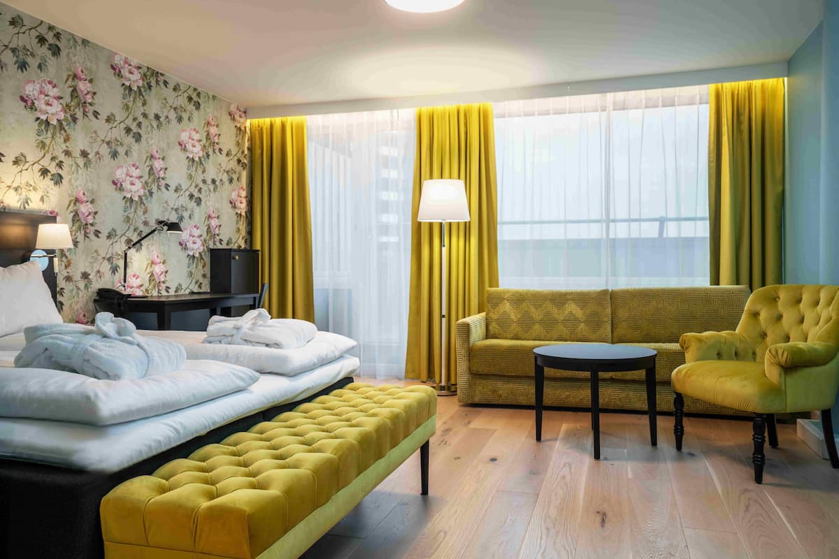 Una habitación de hotel con una cama, un sofá, una silla, una mesita y una lámpara.