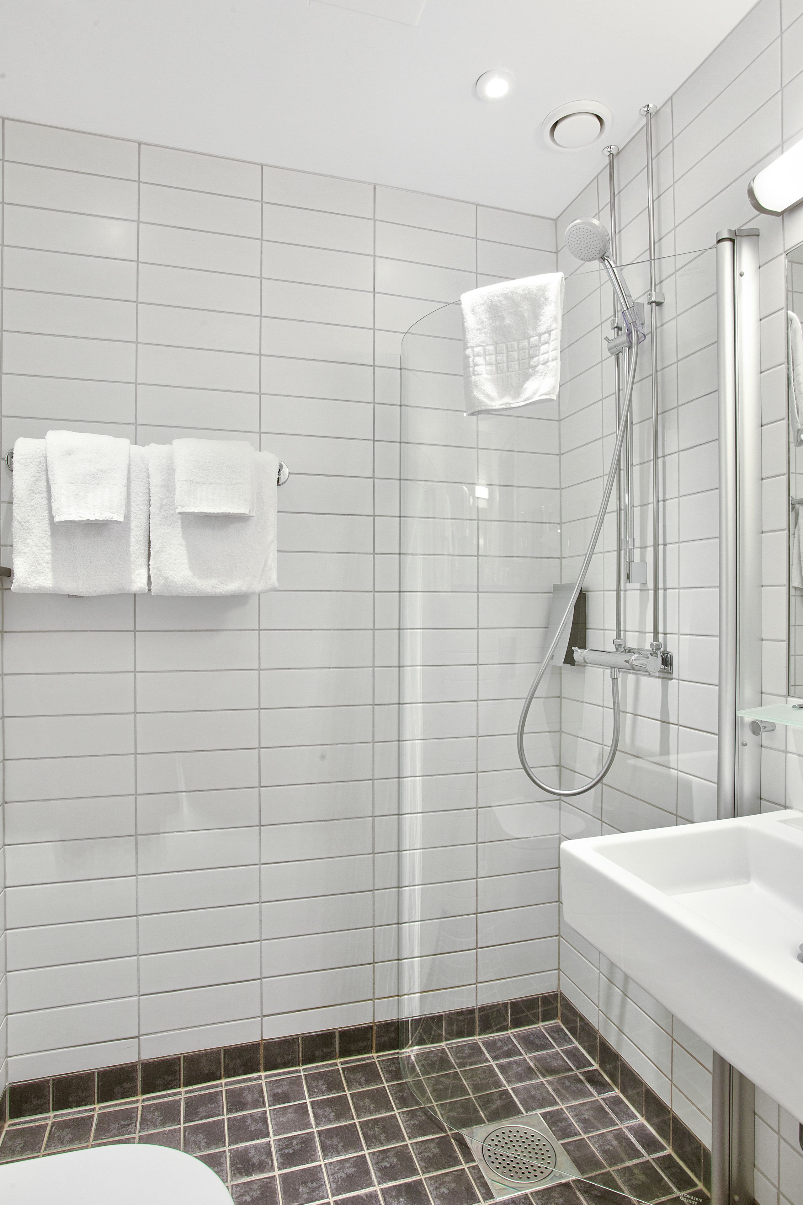Un baño moderno con paredes de azulejos blancos, zona de ducha y lavamanos blanco.