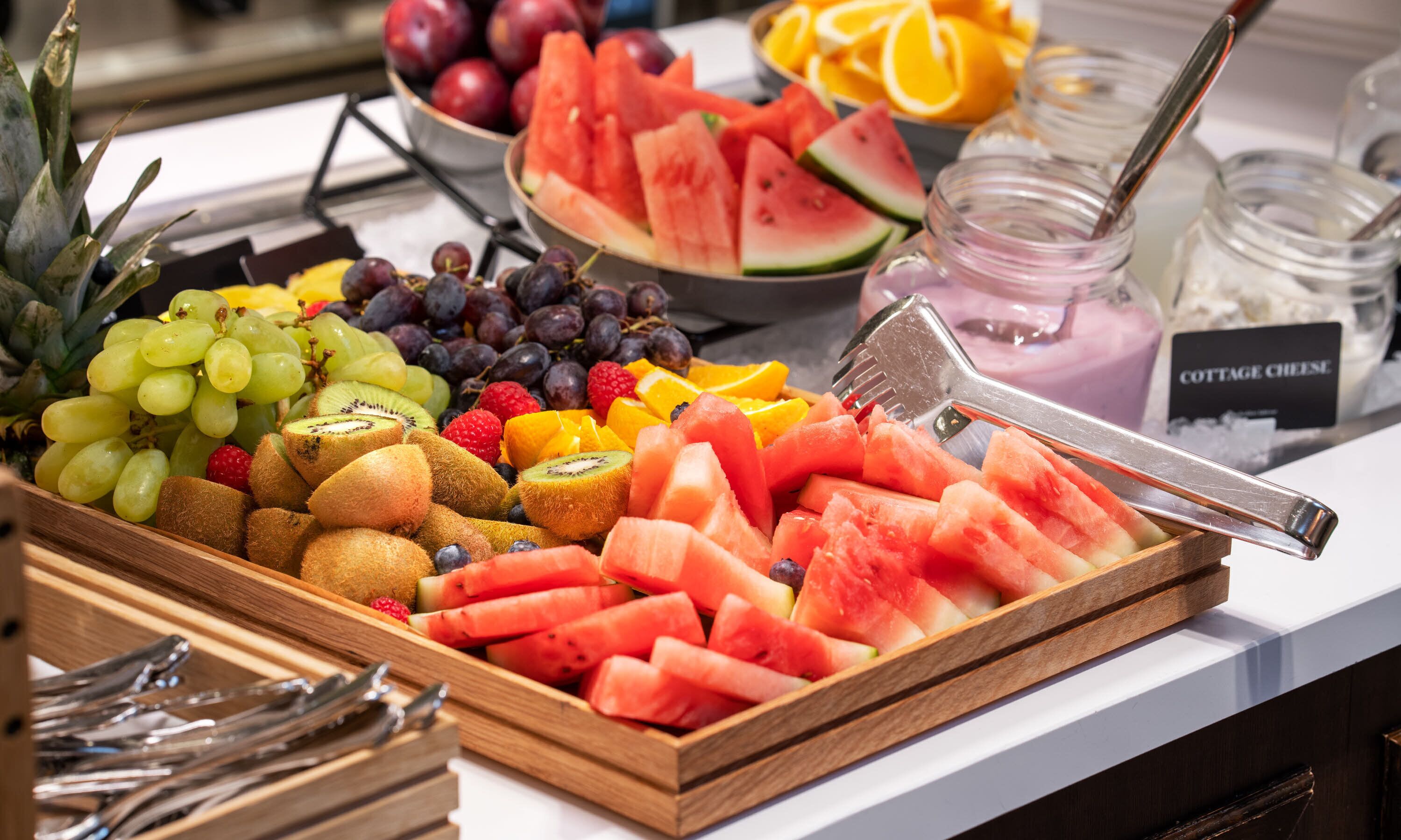 A fruit and cheese platter with various fruits, including grapes, kiwi, watermelon, and oranges, and a jar of cottage cheese.