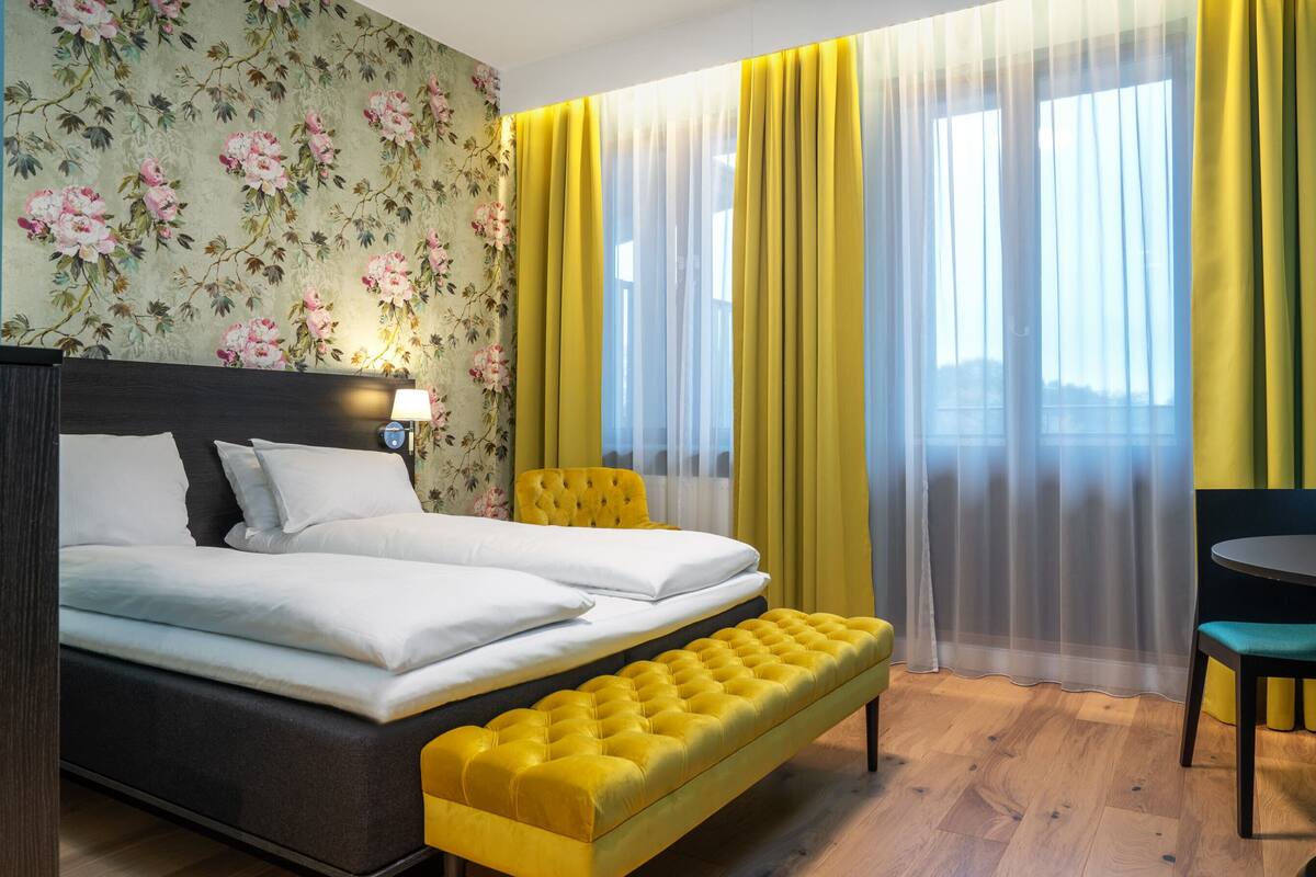 Ein Hotelzimmer mit einem Bett, einem gelben Pouf, einem runden Tisch und einem Stuhl.