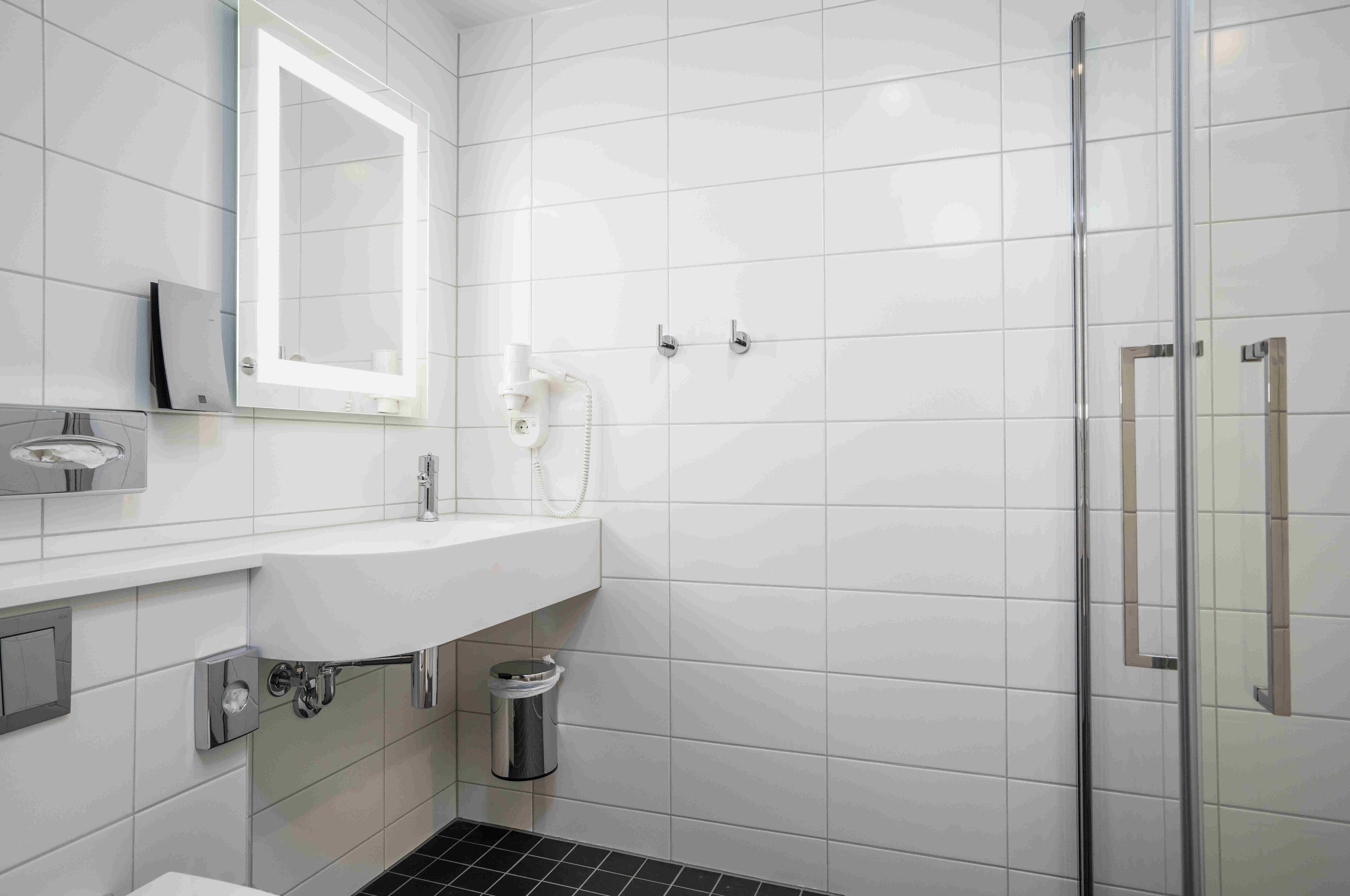 Ein modernes Badezimmer mit einem weißen Waschbecken, einem Spiegel, einer Glasdusche und einem Mülleimer.