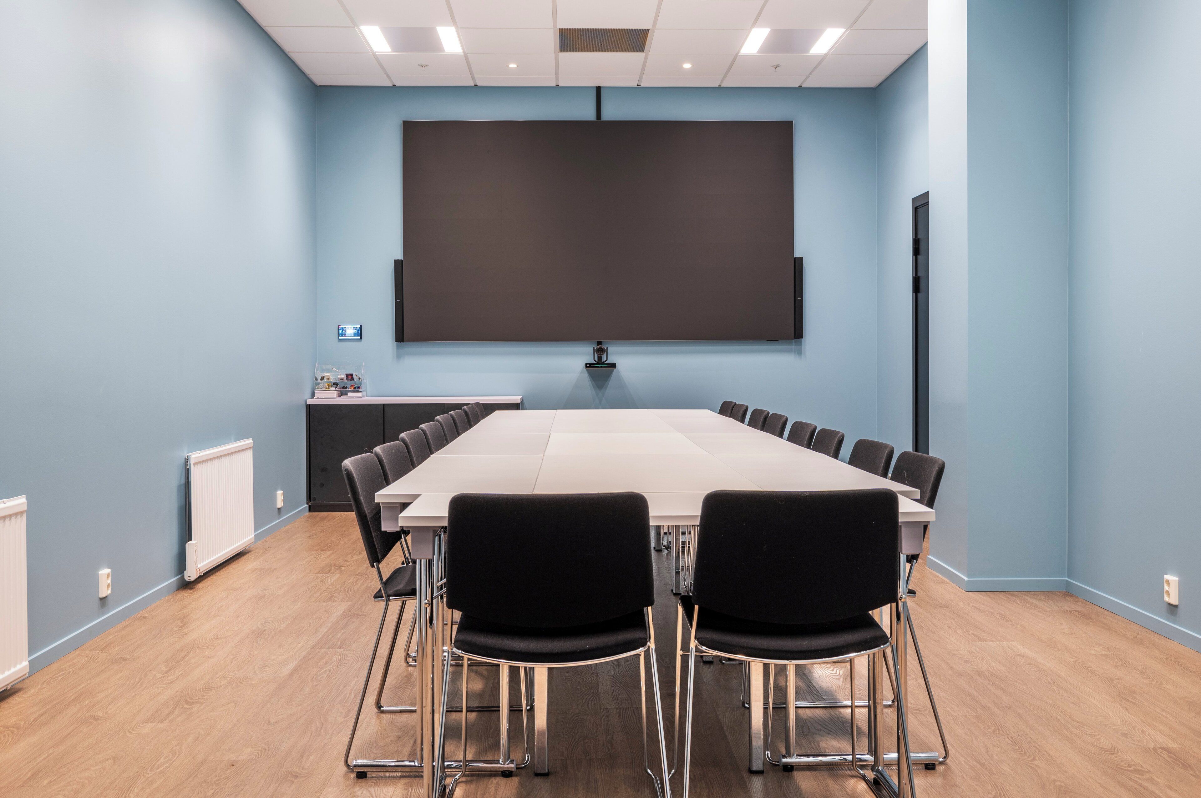 A conference room with a large table, black chairs, a projector screen, and a whiteboard.
