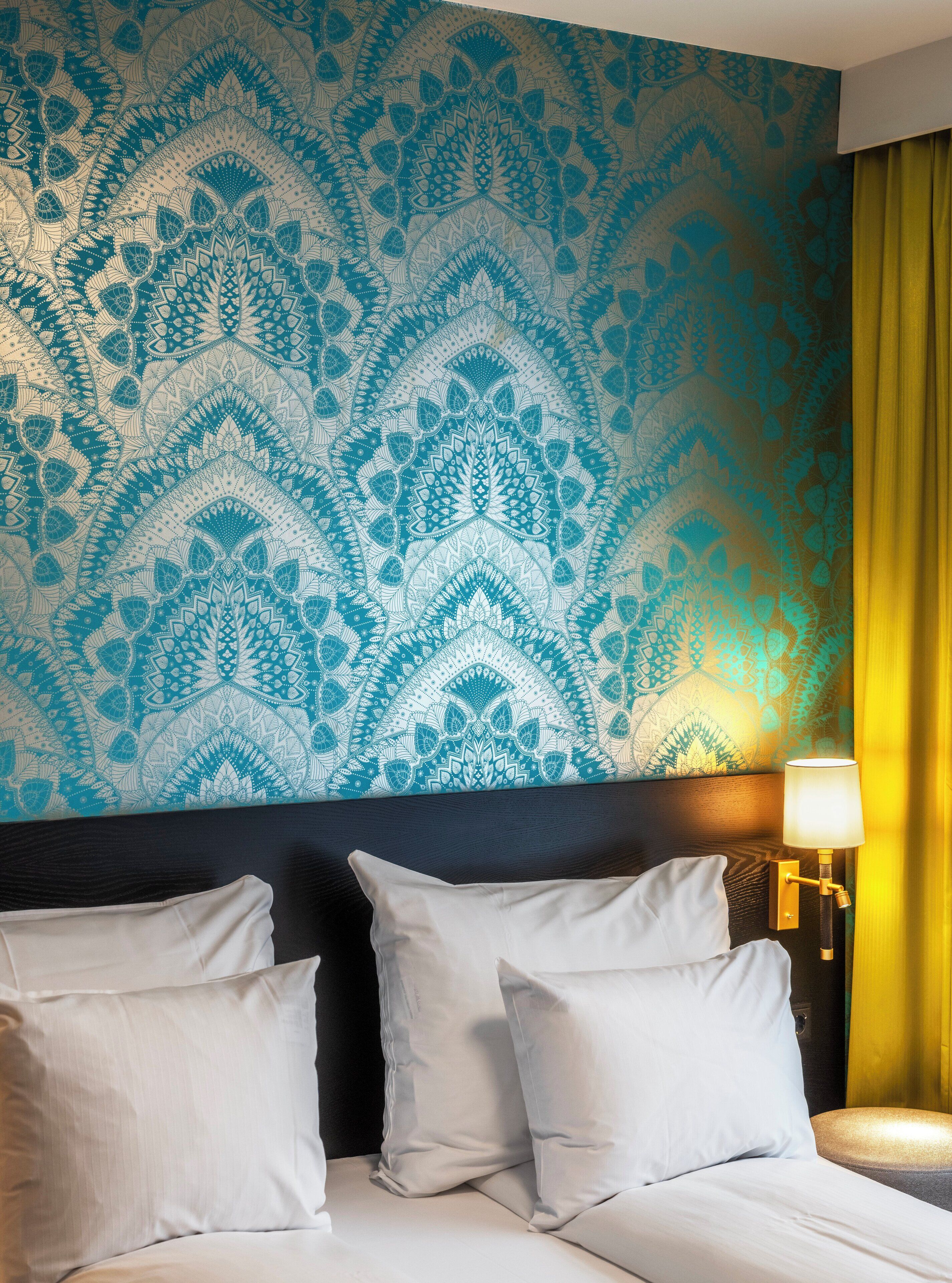 Una habitación de hotel con pared estampada, una cama con ropa de cama blanca y una mesita de noche con lámpara.