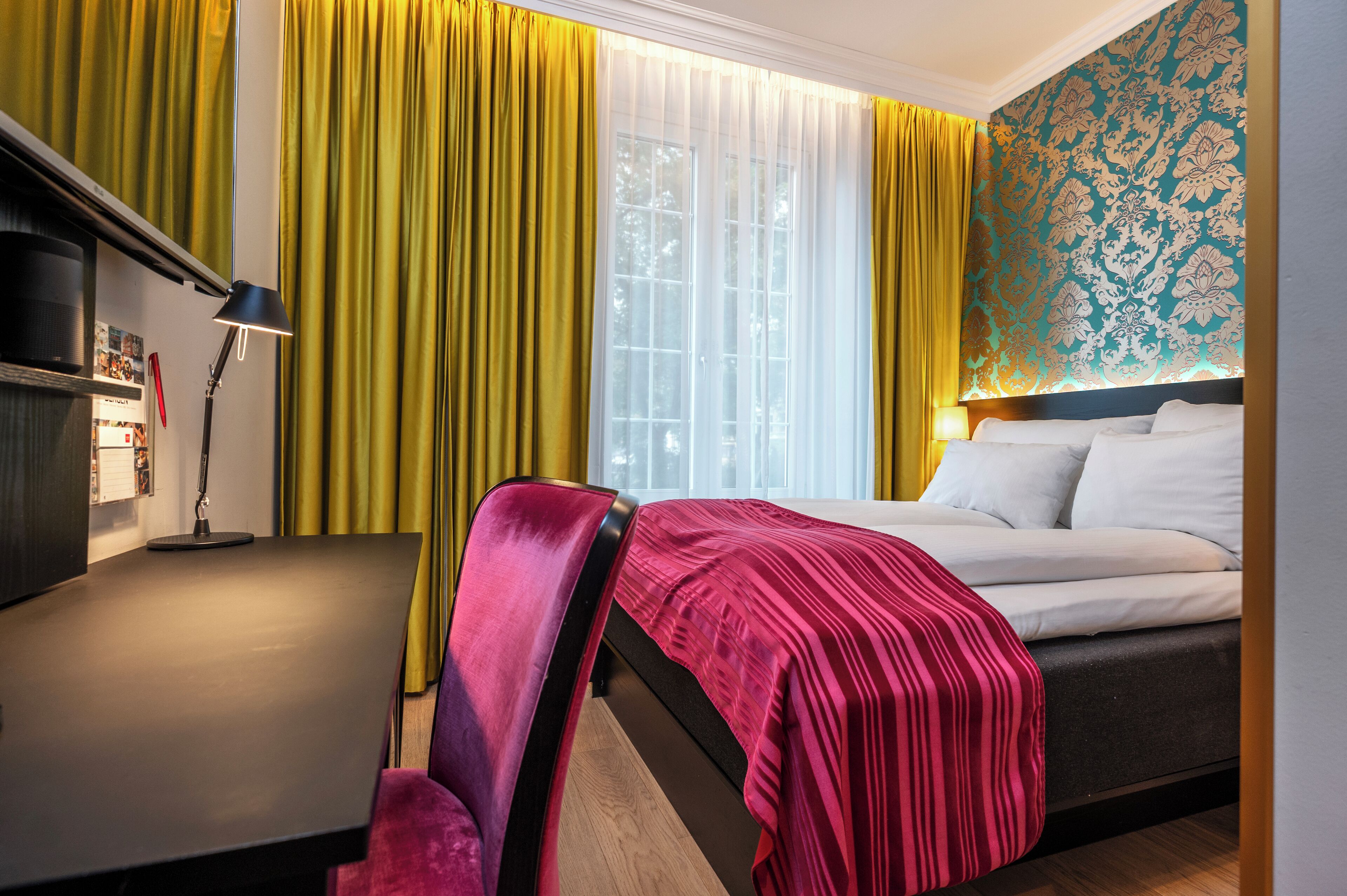 A hotel room with a bed, a desk, a chair, and a window with curtains.