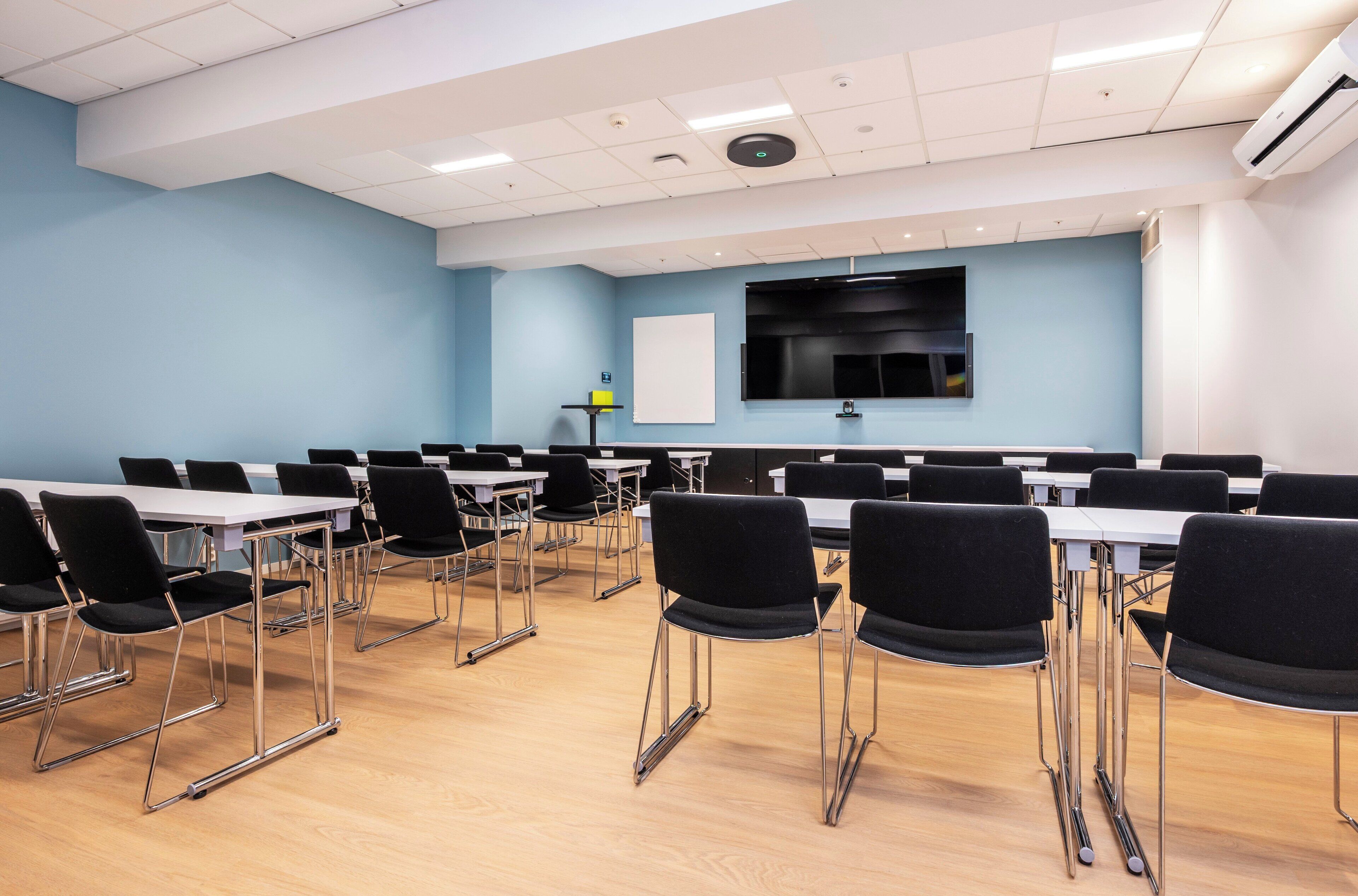 A conference room with tables and chairs, a whiteboard, and a large screen.