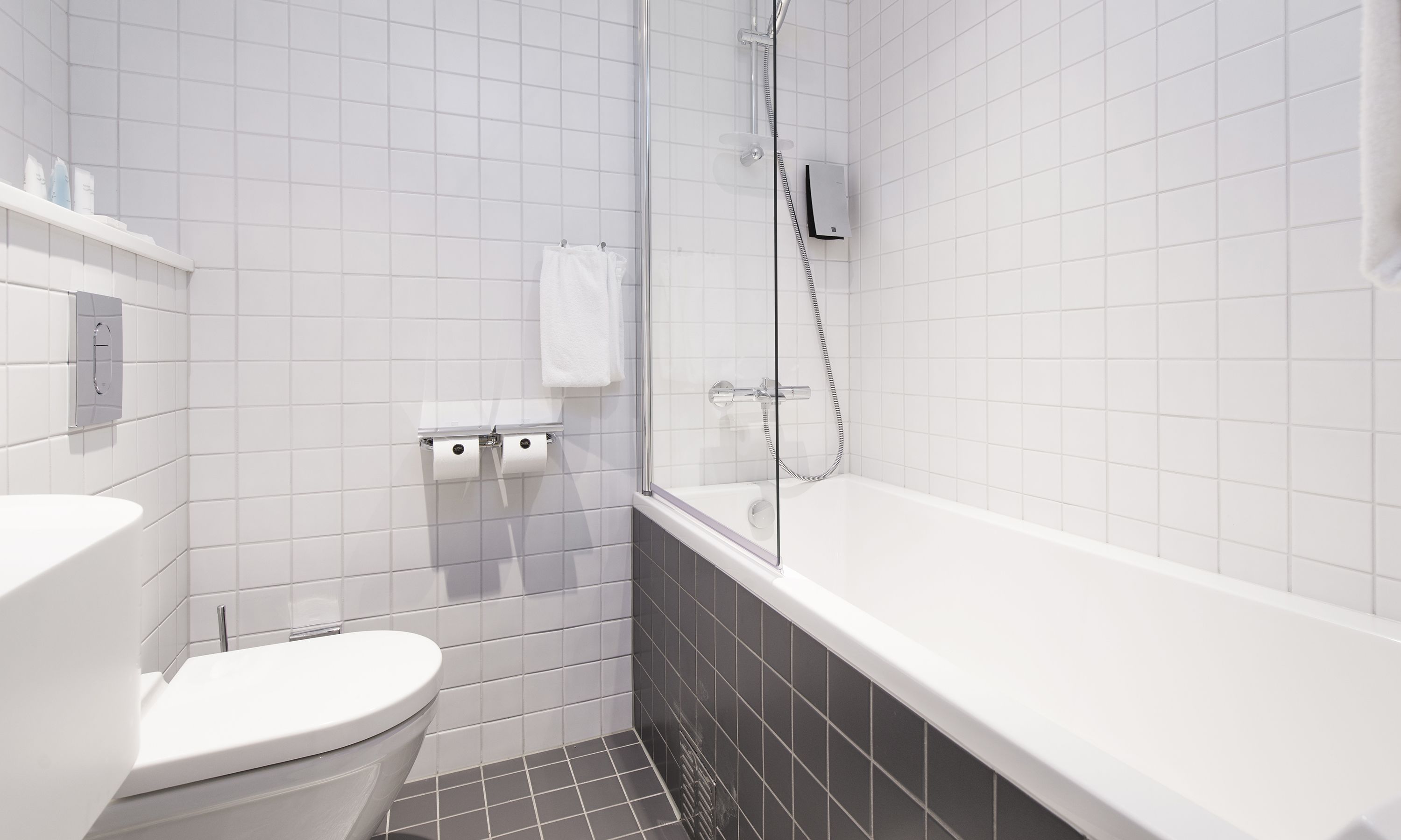 A modern bathroom with a white toilet, a bathtub, and a glass-enclosed shower.