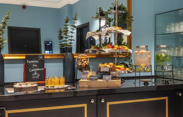 Un bufé de desayuno con diversas opciones de comida y bebidas, un letrero que indica asientos reservados, y un arreglo decorativo de plantas.