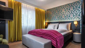 A modern hotel room with a large bed, a bench, a TV, and a patterned wall.