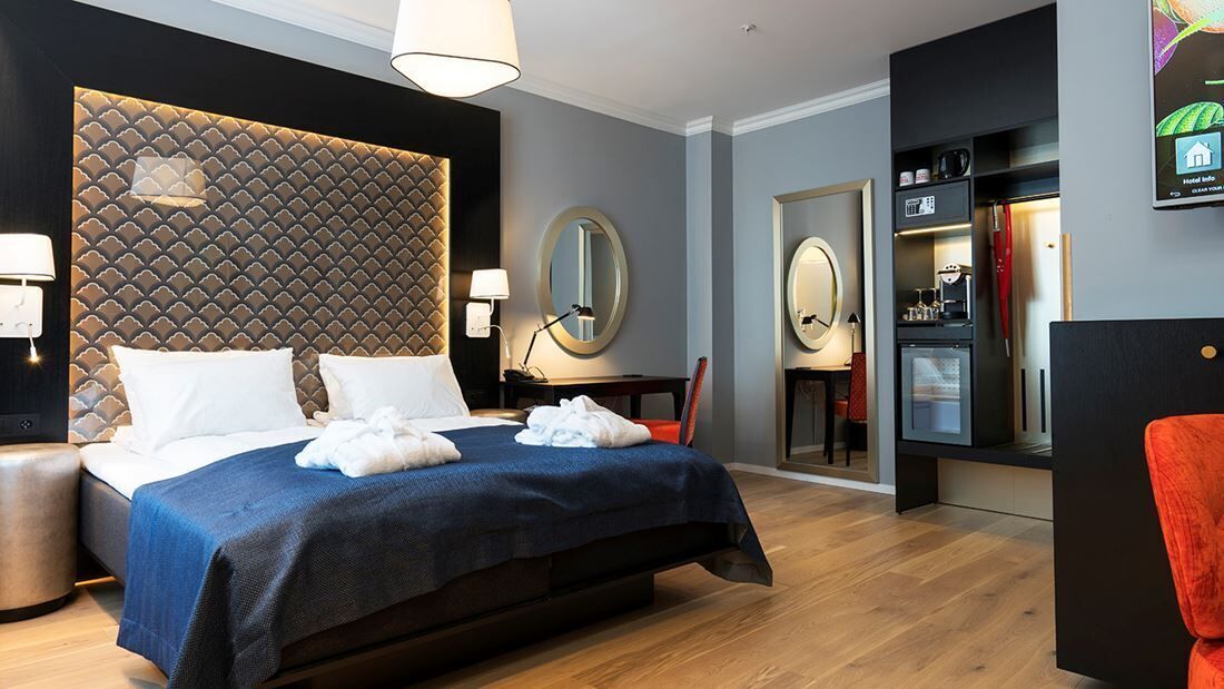 Una habitación de hotel con una cama grande, un escritorio, una silla, un espejo y un televisor.