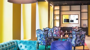 A modern dining area with a round table, colorful patterned chairs, and a tufted blue sofa. - Thon Hotel Spectrum (Oslo)
