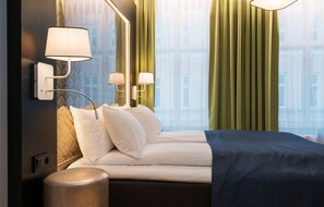 A modern hotel room with a neatly made bed, two wall-mounted lamps, and a large window with green curtains. - Thon Hotel Spectrum (Oslo)