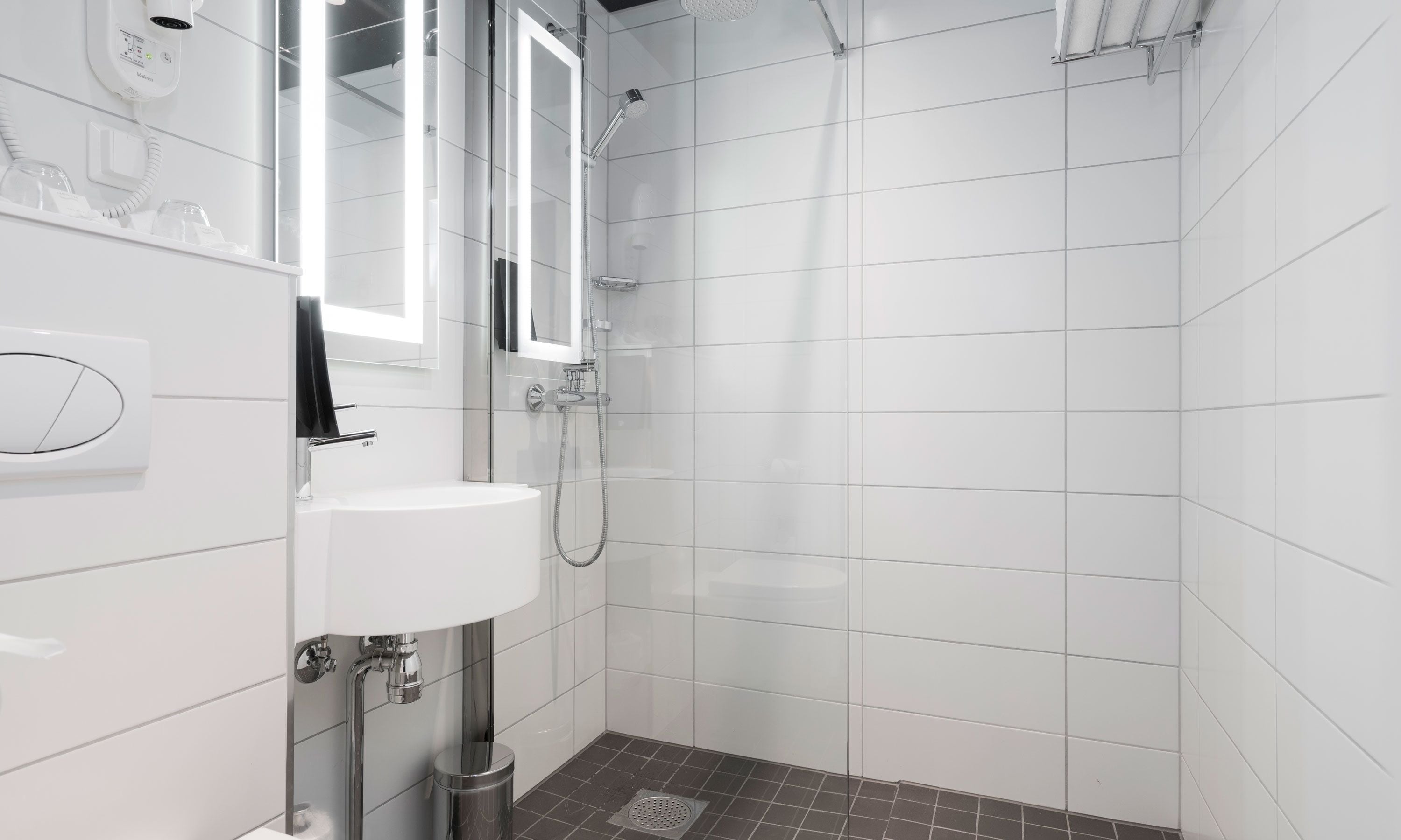 Een moderne badkamer met witte tegels, een wastafel, een spiegel en een douche.