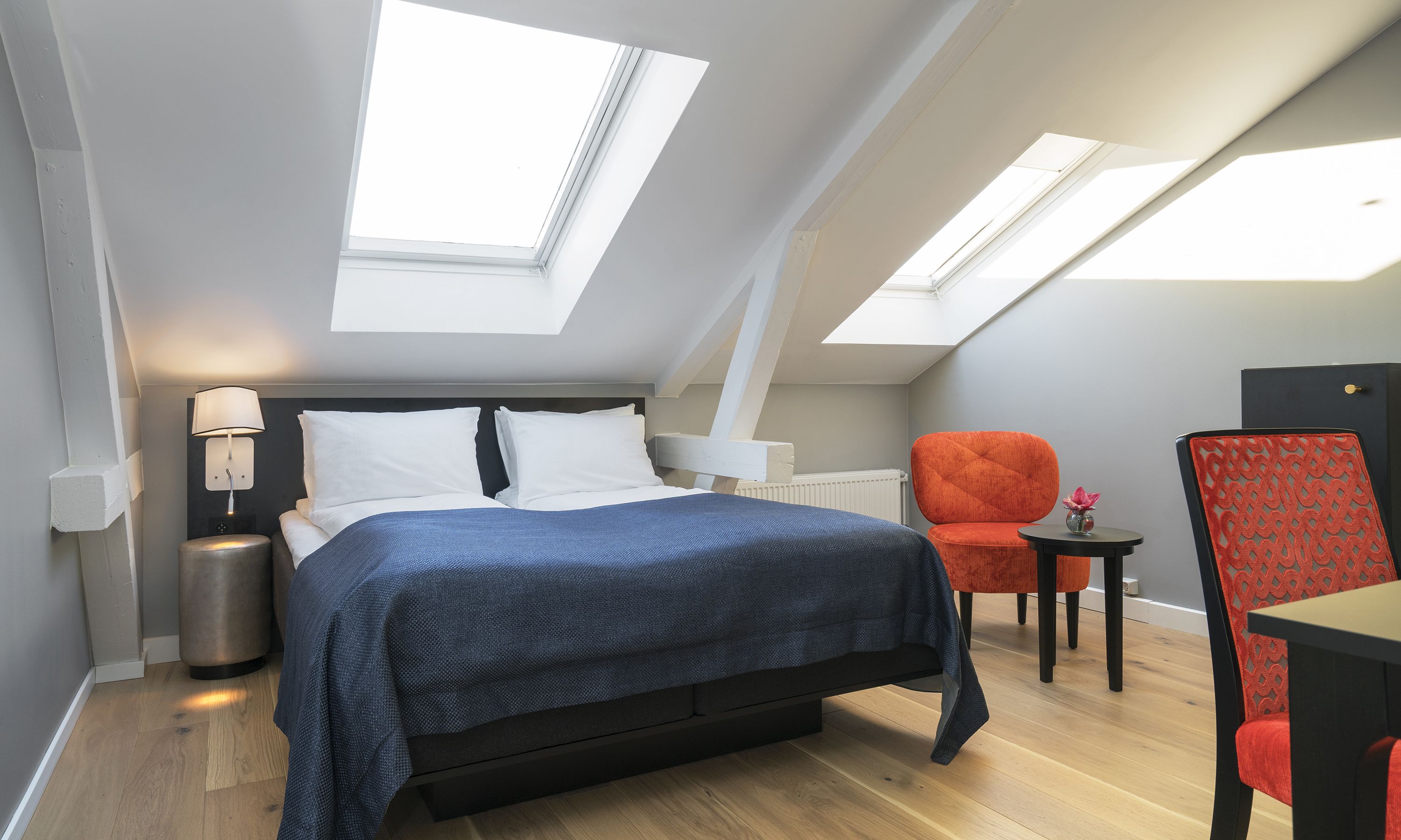 Een moderne slaapkamer met een bed, een nachtkastje, een lamp en twee stoelen.