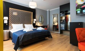 A hotel room with a bed, bedside lamps, a mirror, a desk with a chair, a minibar, and a television.