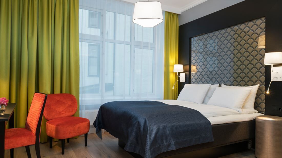 Una habitación de hotel con cama, escritorio, silla y mesita de noche.