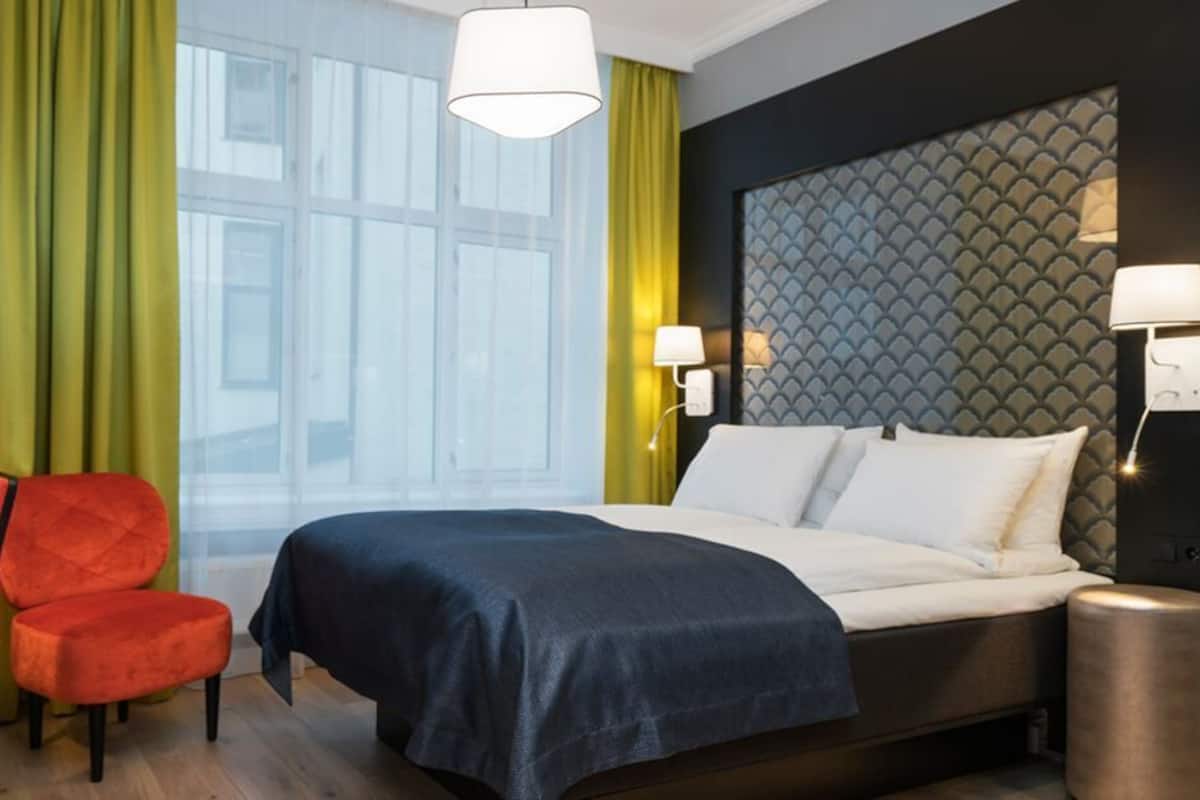 Una habitación de hotel con cama, escritorio, silla y mesita de noche.