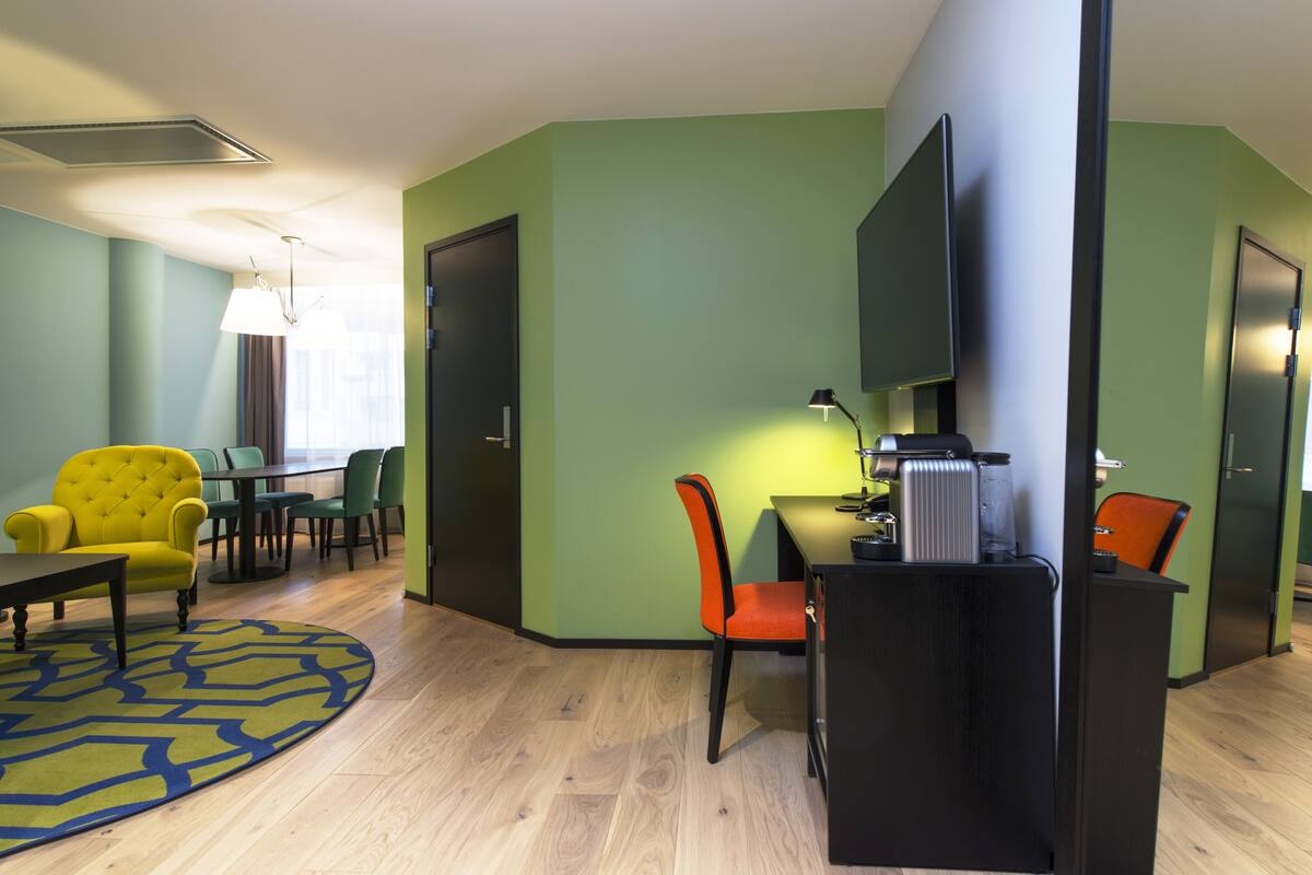 A modern hotel room with a dining area, a flat-screen TV, and a coffee machine.