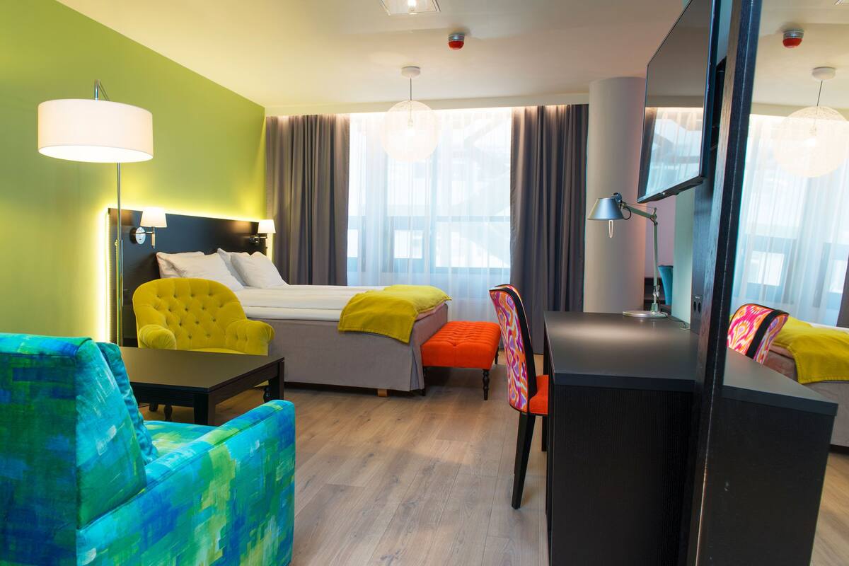 A hotel room with a bed, a desk, a chair, and a sofa.