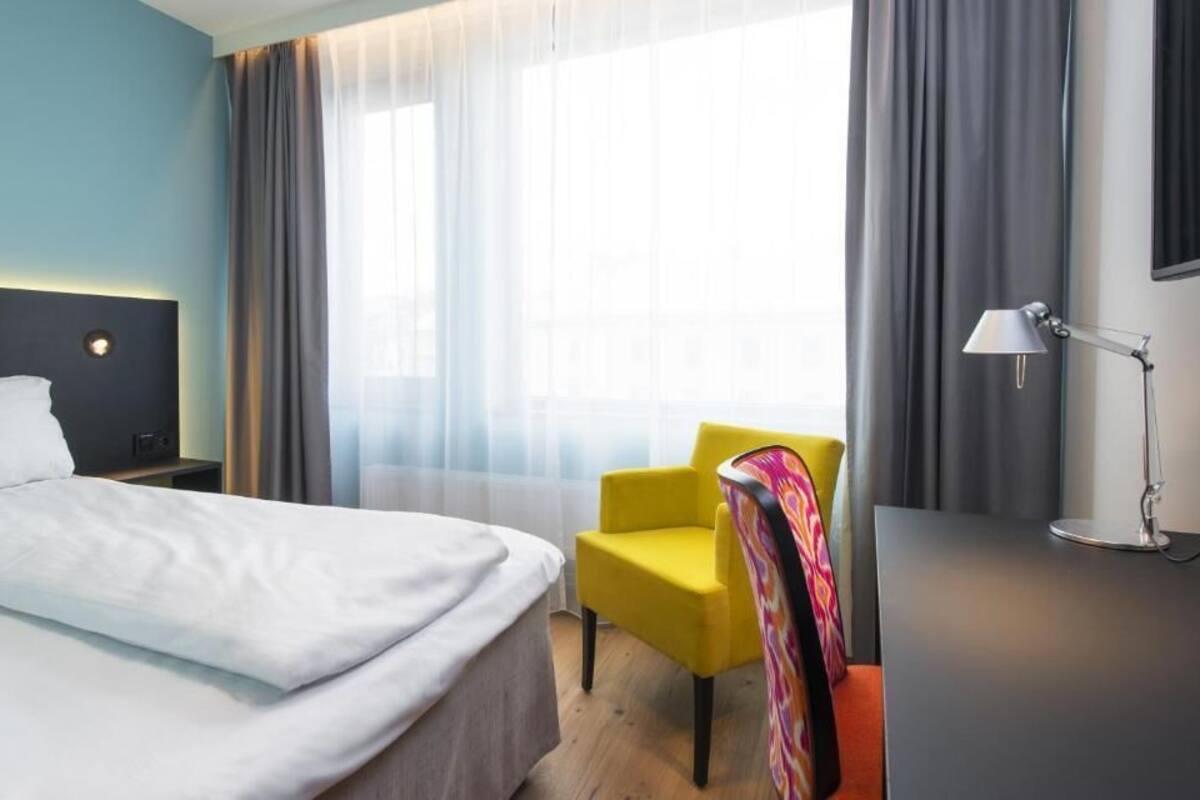 A hotel room with a bed, a chair, a desk, and a lamp.