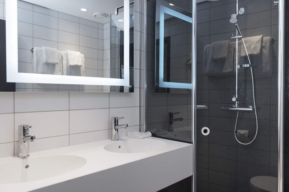 Un baño moderno con dos lavamanos, un espejo grande y una zona de ducha con cerramiento de vidrio.