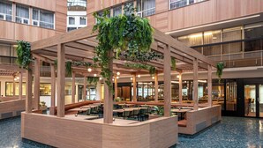 A modern indoor space with wooden structures and seating areas, featuring a central island with a bench and tables. - Thon Hotel Vika Atrium (Oslo)