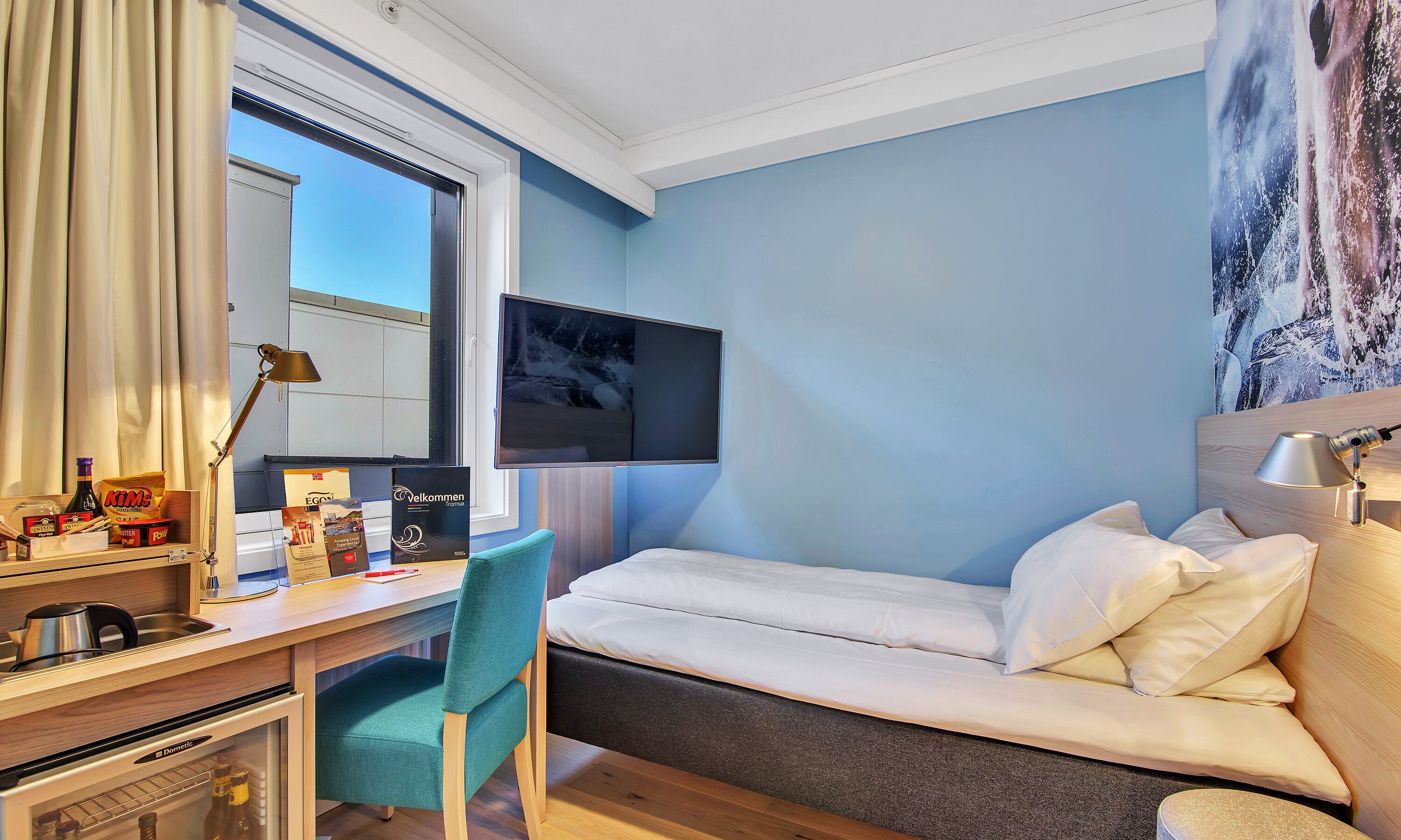 A hotel room with a bed, desk, chair, and a television mounted on the wall.