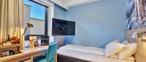 A hotel room with a bed, desk, chair, and a television mounted on the wall.