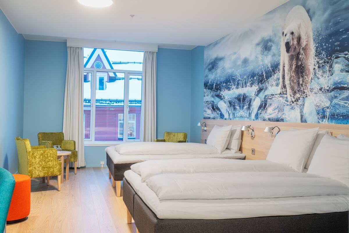 Et hotelværelse med to senge, et skrivebord med stol, et fjernsyn og et vindue med udsigt til en bygning.