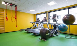 Un gimnasio con cintas de correr, balones de ejercicios y bandas de resistencia rojas.