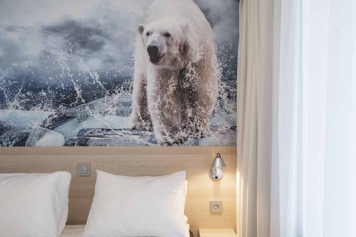 A hotel room with a large polar bear painting on the wall, a wooden headboard, a bedside lamp, and a white bed.