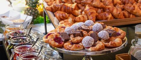 A buffet with various pastries, including croissants and fruit tarts, and several jars of jam.