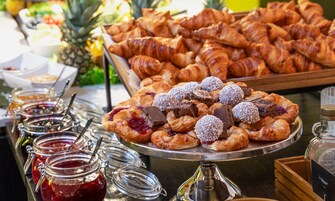 Un bufé con diversas opciones de bollería, incluyendo croissants y tartaletas de fruta, además de varios frascos de mermelada.