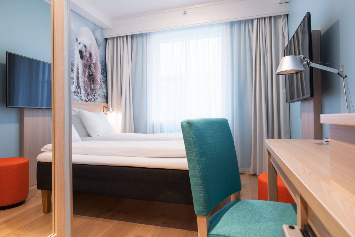 Et hotelværelse med seng, skrivebord, stol, tv og et billede på væggen.
