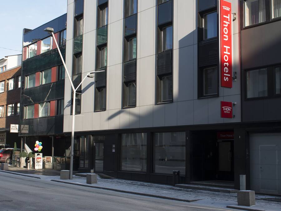 A modern hotel building with a prominent red sign, large windows, and a clean, urban street view.