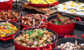 Un bufé con diversos platos, incluyendo salchichas, patatas asadas y champiñones.