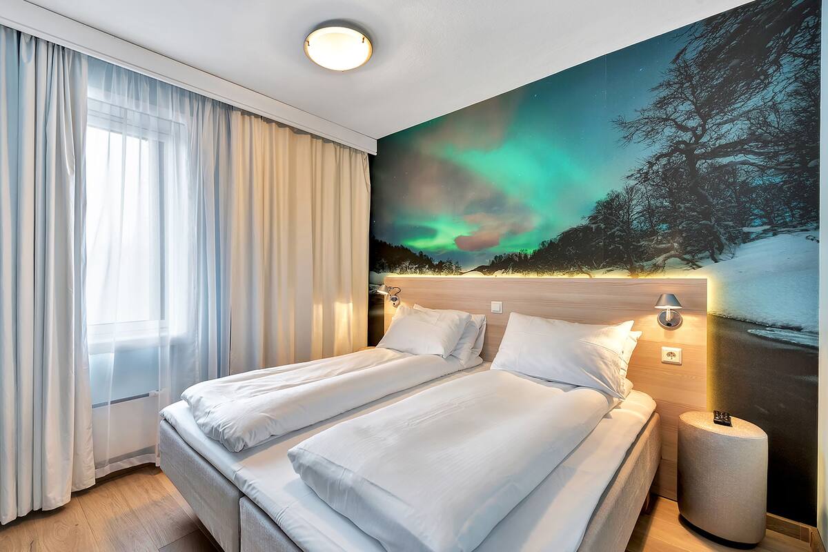 Et hotelværelse med en seng, et natbord, en lampe og et billede af nordlys.