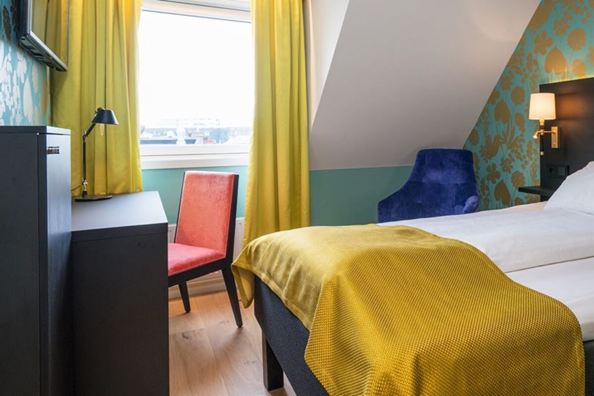 Una habitación de hotel con una cama, un escritorio, una silla y una ventana con cortinas.