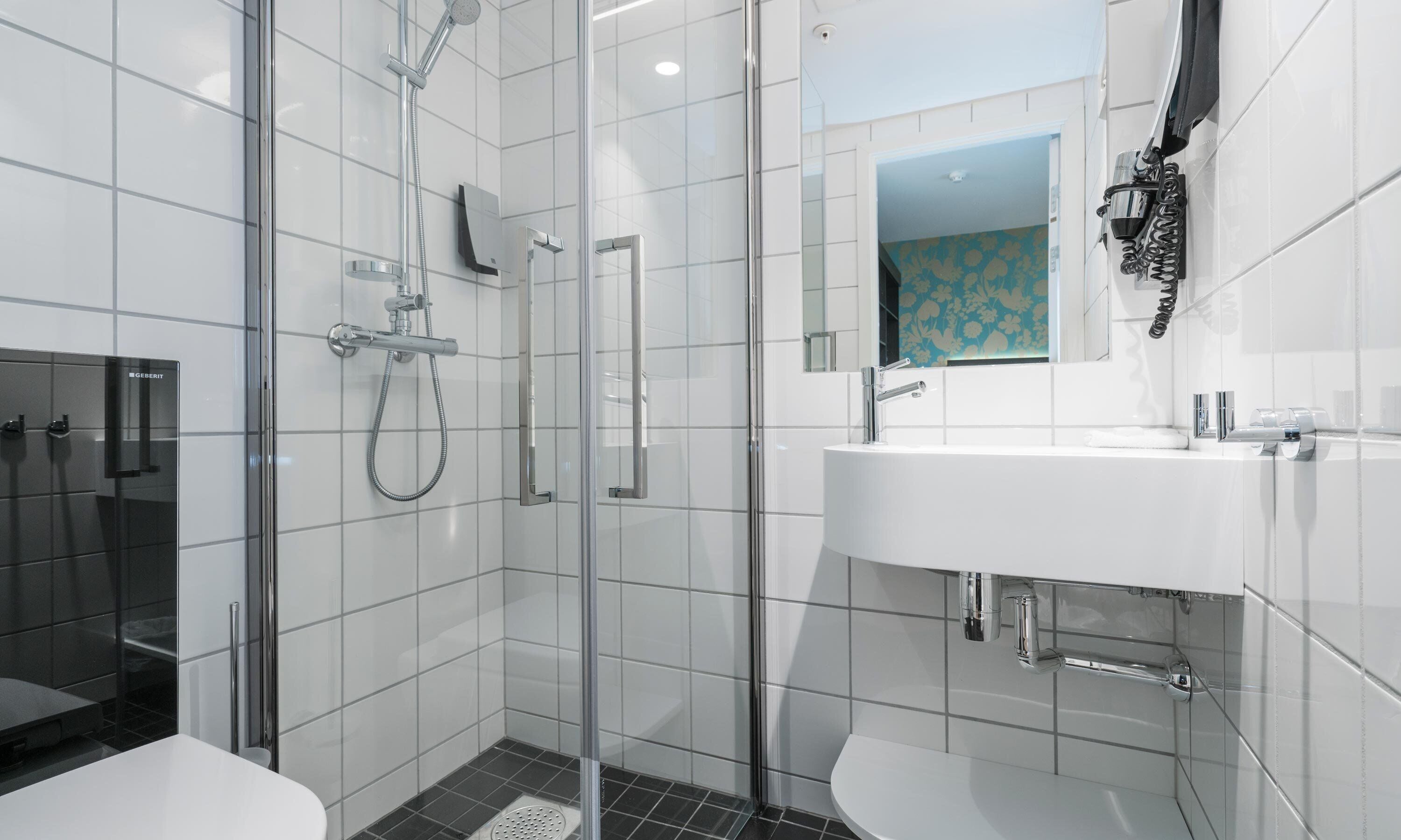 Un baño moderno con ducha de vidrio, un lavamanos blanco con grifería cromada y un espejo pequeño sobre el lavamanos.