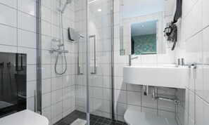 Un baño moderno con ducha de vidrio, un lavamanos blanco con grifería cromada y un espejo pequeño sobre el lavamanos.
