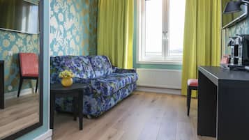 A room with a sofa, a small table with a vase, a red chair, a desk, and a window with curtains.