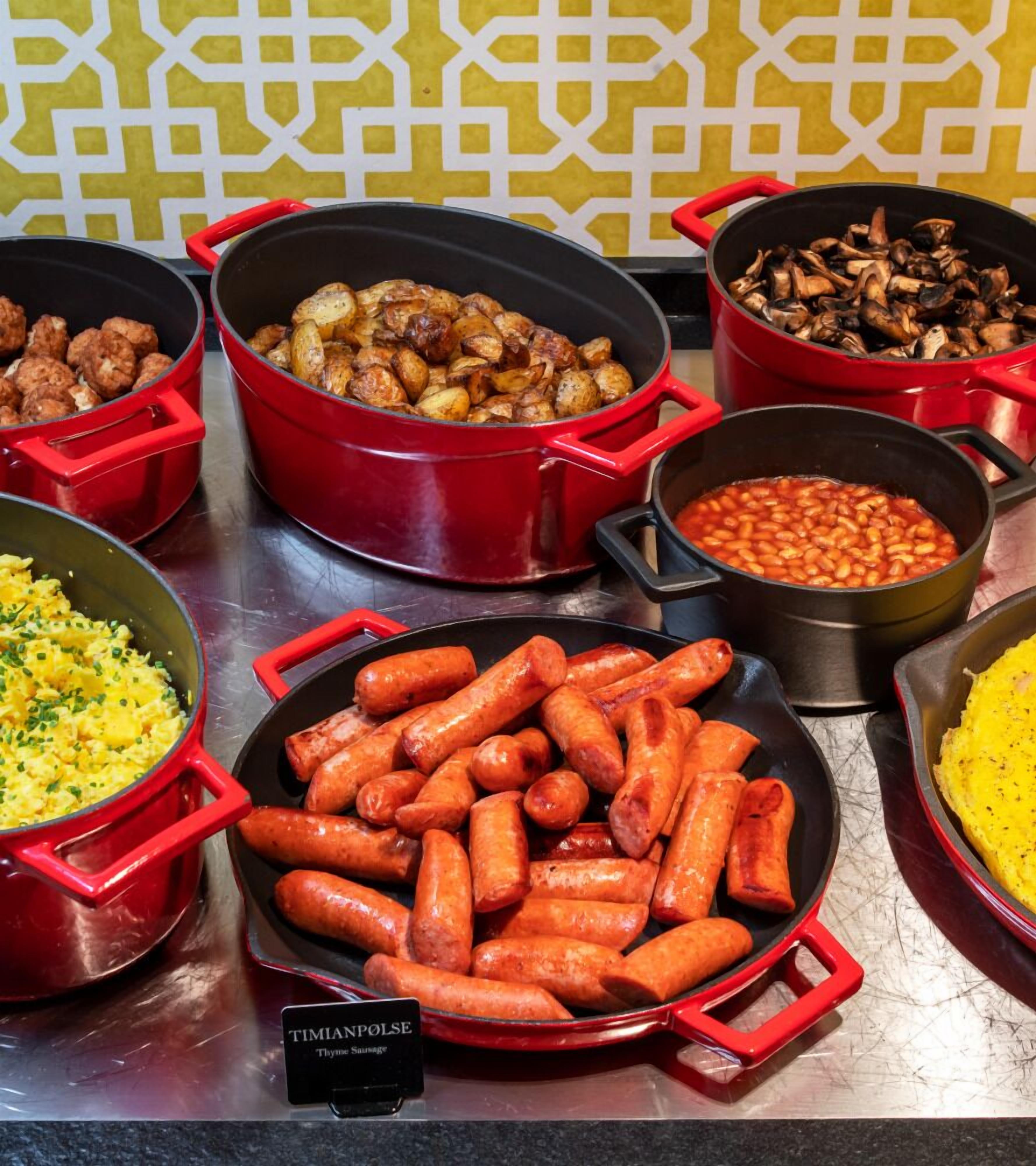 Een buffet met diverse gerechten, zoals worstjes, geroosterde aardappelen, bonen en roerei.