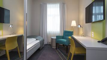 Una habitación de hotel con cama, dos sillas, escritorio, lámpara, televisión y ventana con cortinas.